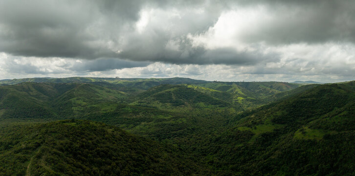 Aerial view of rolling hills and valleys blanketed in lush greenery under a dramatic, cloudy sky, KwaMvulo, Eastern Cape, South Africa.
