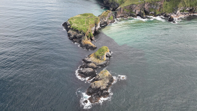 Aerial view of the rocky outcrop and verdant cliffs meet the restless ocean, a stark contrast against the deep blue depths, Ballycastle, Causeway Coast and Glens, United Kingdom.