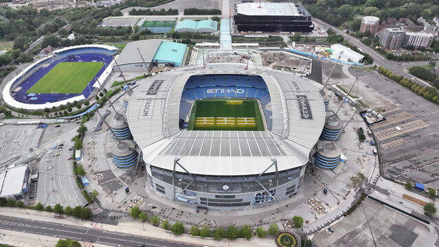 Aerial view of the Etihad Stadium, with its distinctive blue accents and sprawling grounds, stands proudly amidst a tapestry of urban structures, Manchester, England, United Kingdom.
