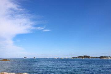 Obraz premium Calm blue waters of the Mediterranean sea with distant yachts near Beaulieu-sur-Mer, Peaceful seascape at the French Riviera with rocky coast and wide open sky