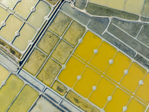 Aerial view of geometric salt pans shimmer with vibrant hues, creating a mosaic of earth tones under the French sun, Guerande, Bretagne, France.