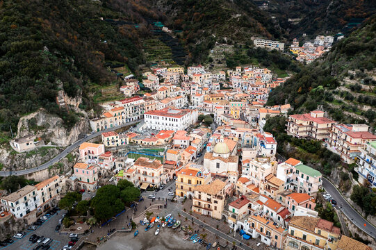 Aerial view of clustered buildings with terracotta roofs cascade down to the harbor, nestled between the verdant hills and the Tyrrhenian Sea, Cetara, Campania, Italy.