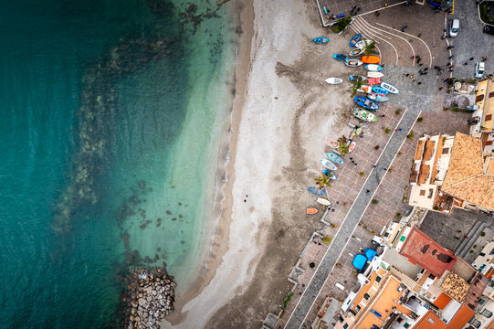 Aerial view of azure waters meet the sandy shore, boats lined along the promenade contrasting with the warm tones of the buildings, Cetara, Campania, Italy.