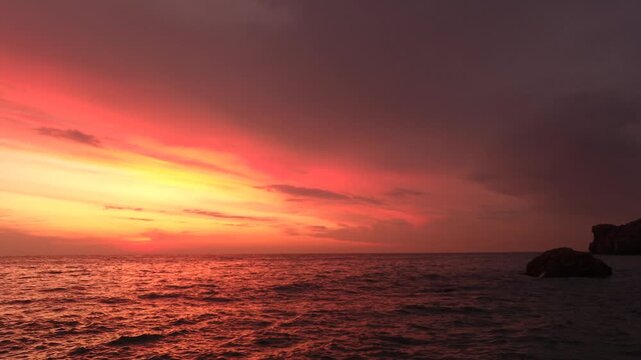 Sunset, ocean, seascape, fiery red and purple sunset over open ocean waves near rocky coastal cliffs.