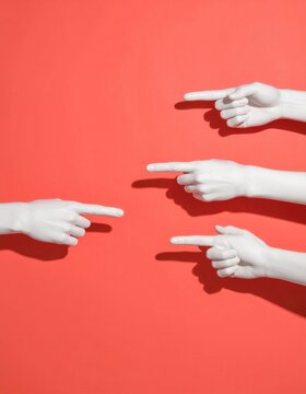 Białe dłonie manekin&oacute;w wskazujące na siebie na jaskrawym czerwonym tle, symbolizujące oskarżenie, konflikt społeczny oraz wzajemne obwinianie.