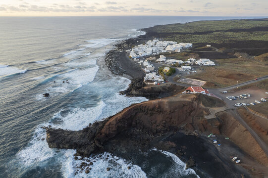 Aerial view of the stark black volcanic landscape meets the crashing turquoise waves near the white-washed village of El Golfo, El Golfo, Canary Islands, Spain.