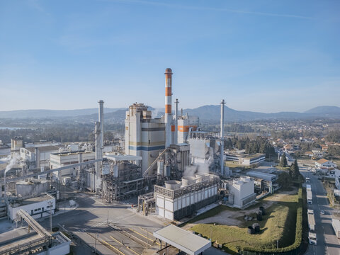 Aerial view of a massive DS Smith Paper mill industrial complex with towering chimneys reaching towards the clear blue sky, Deocriste, Viana do Castelo, Portugal.