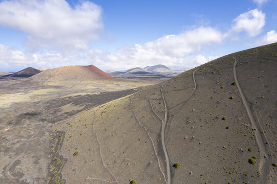 Aerial view of volcanic cones punctuate the arid landscape of Caldera de Los Cuervos under a vast sky, trails etching paths on the slopes, Tinajo, Canary Islands, Spain.