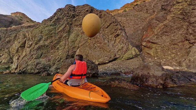 Kayaking adventure coastline man in orange kayak paddling near majestic rocky cliffs during a peaceful afternoon at sea