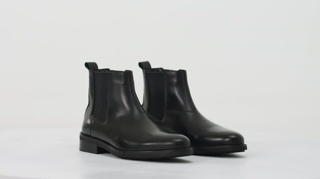 Stylish classic black leather chelsea boots turning in a photo studio, set against a pristine white backdrop