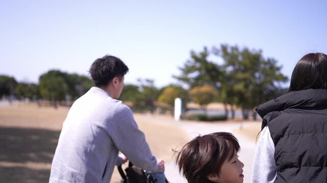 A woman wearing a black jacket and a vest is walking with a baby stroller. She is smiling and she is enjoying her time outdoors