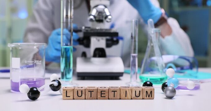 Miniature wooden cubes on laboratory table form term Lutetium. Female chemist examines sample carefully through high-precision microscope