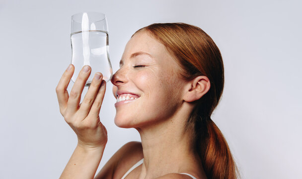Smiling redhead woman holding a glass of water to her face