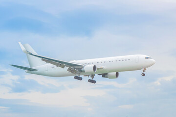 Obraz premium A white empty mockup wide-body passenger plane against a background of white clouds and blue sky with a extended landing gear- coming in for landing or immediately after takeoff. Сoncept of air travel