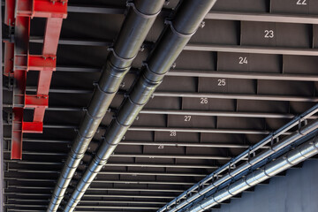 Fototapeta premium Steel bridge infrastructure pipelines ducts installed metal girders numbered beams under roadway. Industrial engineering structure modern transport network utilities integrated construction framework