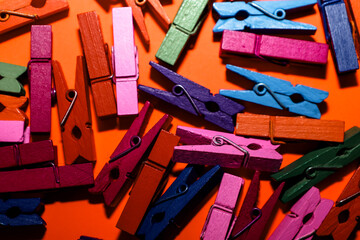 Multicolored wooden clothespins are chaotically scattered on a bright orange background, creating a dynamic and vivid texture. This abstract composition symbolizes household life,