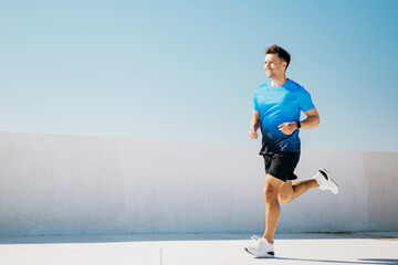 Man runs on a sunny day near a white wall in a sports outfit while enjoying the outdoor activity