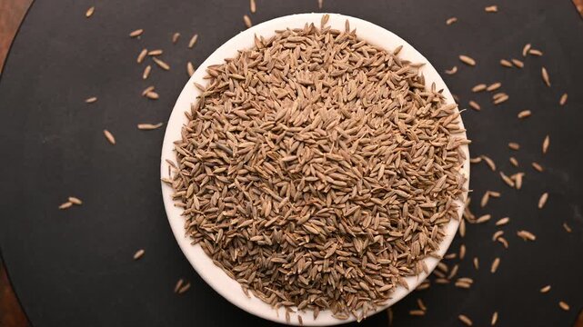 Top View of Cumin Seeds (Jeera) in White Bowl on Black Background &ndash; Rotating Footage