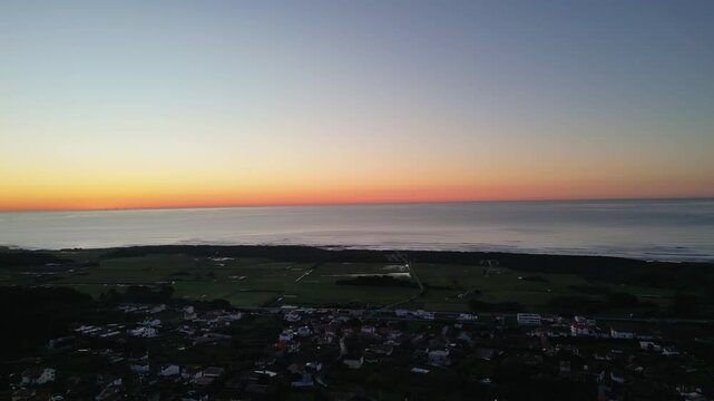 Orbit aerial view of the sunset over the sea with Afife village behind, revealing coastline, houses and warm golden light across the landscape.