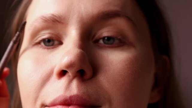 Close up of a young woman using a professional spoolie brush to comb and shape her eyebrows. Detailed view of a natural eyebrow grooming and makeup routine