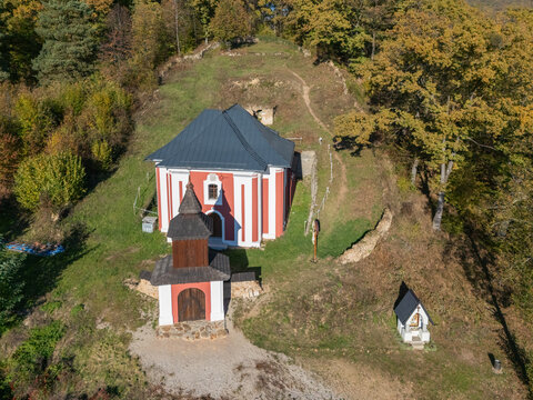 Aerial view of the Calvary Roznava, with a red and white church nestled amid autumn trees, creating a striking contrast of color and form, Roznava, Kosice Region, Slovakia.