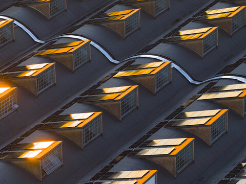 Aerial view of the rhythmic pattern of rooftop windows reflecting the warm glow of sunlight against the cool, dark metal, Roma, Lazio, Italy.