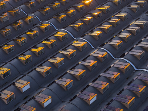 Aerial view of rows of dark curved roofs, punctuated by numerous skylights reflecting the warm glow of the setting sun, Roma, Lazio, Italy.
