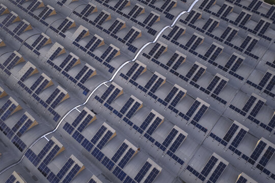 Aerial view of uniform solar panels glinting under the sun, arranged in neat rows on a vast rooftop, Roma, Lazio, Italy.