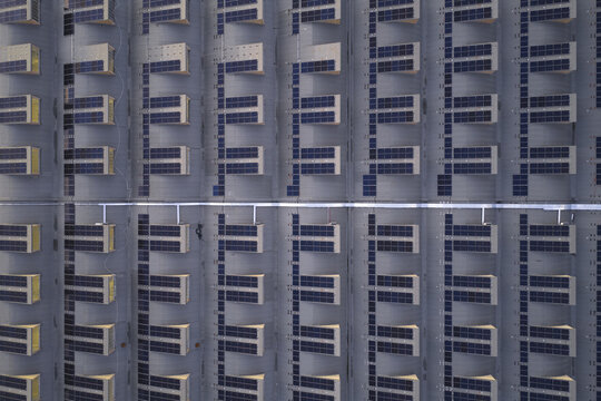 Aerial view of rows of solar panels reflecting the sky's soft light, creating a grid-like pattern of dark blues and pale grays, Roma, Lazio, Italy.