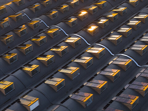 Aerial view of sunlight glinting off the many windows of a dark, patterned roof, creating a warm glow against the cool shadows, Roma, Lazio, Italy.
