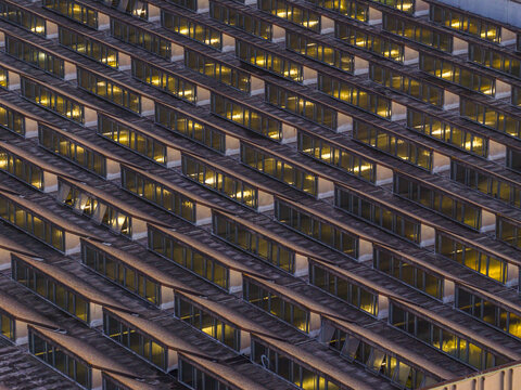Aerial view of warmly lit windows glow like honeycombs against the cool, shadowed facade of a modern building, Roma, Lazio, Italy.