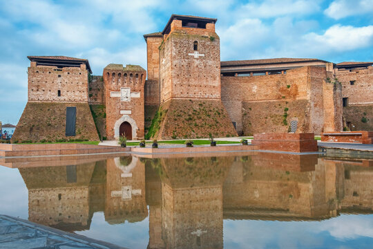 Brick towers and defensive walls of Castel Sismondo in Rimini rise behind shallow reflecting pool, Emilia Romagna, Italy. Medieval fortress. Italian architecture. Travel and tourism destination