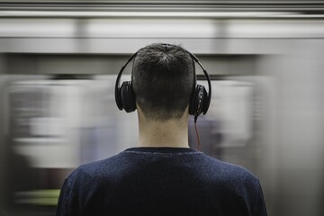 Young man with headphones waits for fast moving subway train from behind © SKILLTAKES.COM