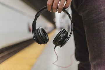 Person holding black over ear headphones while waiting on subway platform © SKILLTAKES.COM