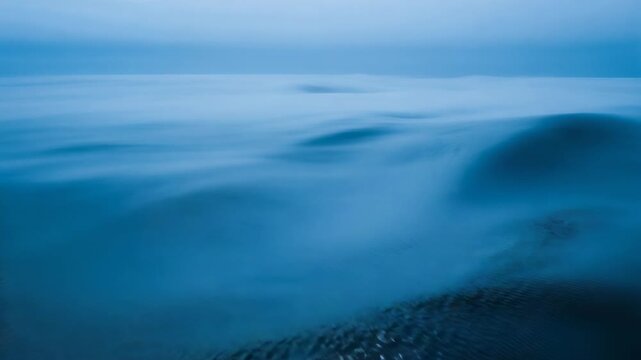 Rolling ocean surface forming low swell from left and ripples at open sea, with specular highlights