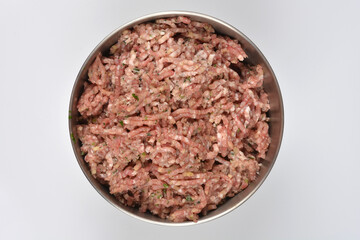 An overhead shot of a stainless steel bowl filled with freshly ground raw pork, mixed with seasonings and herbs, ready for making sausages, set on a bright white background