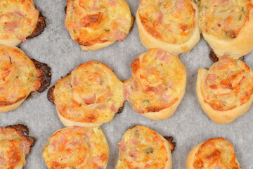 Top view of golden brown baked puff pastry rolls with cheese cream, cheese and ham filling arranged on white baking paper after coming out of the oven