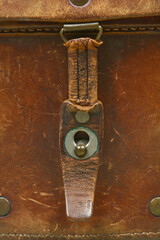 A detailed close-up of a weathered brown leather strap and metal stud closure on a vintage binoculars case showing worn texture and stitching