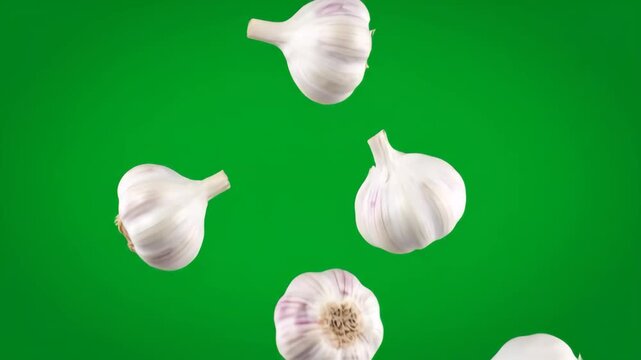 Fresh garlic bulbs falling in slow motion against a vibrant green screen, ideal for culinary and cooking projects.