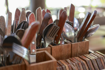 Close up of rustic cutlery with wooden handles in holder. An organized set of forks, spoons, and...