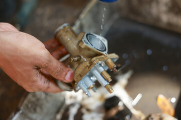 Focused mechanic with dirty hand doing careful maintenance. Close up detail of cleaning vintage motorcycle carburetor, motor part for repair in garage