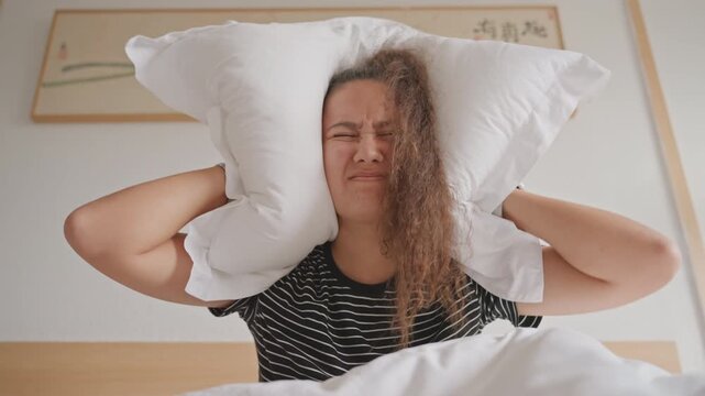 Resigned woman in hotel bed covering face. Buries head beneath pillow and duvet in weary surrender closed eyes, defeated posture, white sheets, bedside art, soft neutral decor, candid portrait