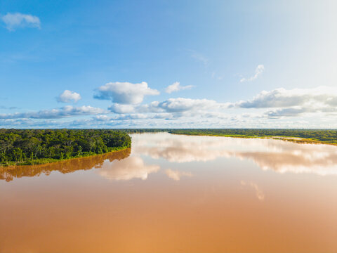 Aerial view of the muddy river reflecting the sky, flowing through the lush green forest, Leticia, Amazonas, Colombia.