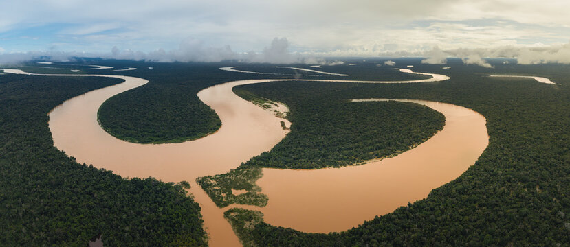 Aerial view of muddy river snaking through a dense, emerald jungle under a cloudy sky, Leticia, Amazonas, Colombia.