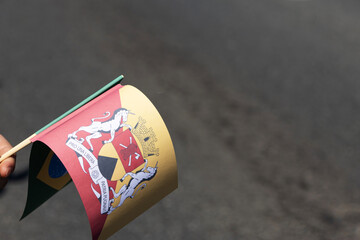 A hand holds paper flags of Sorocaba and Brazil. The state's coat of arms, featuring unicorns and...