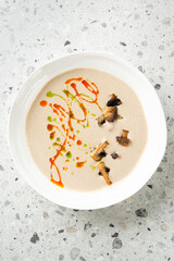 Creamy mushroom soup in a white bowl, garnished with sautéed mushroom pieces and swirls of herb...