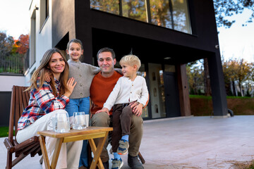 Fototapeta premium Parents with their young children smiling and posing for the camera, sitting on a private terrace of their modern house, representing family lifestyle and togetherness