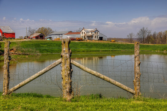 Farm Through a Weathered Fence.  A weathered wire fence stretches across the foreground, creating a natural frame for the farmstead beyond.