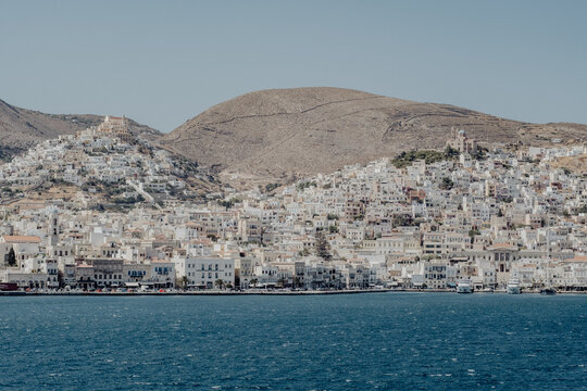 Mediterrane K&uuml;stenstadt vor kahlem H&uuml;gel und ruhigem Meer bei klarem Sommerlicht