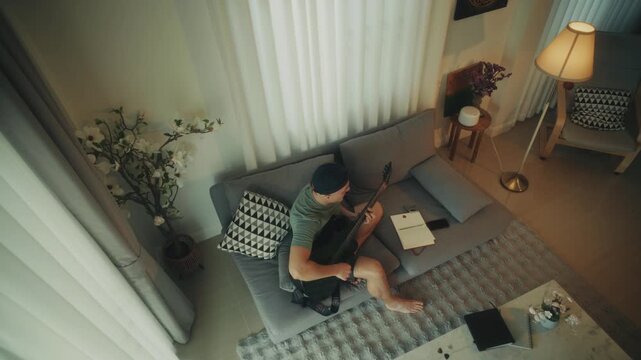 Man Creating Music. Person Sitting Barefoot Crafting Tunes With Acoustic Guitar And Notebook